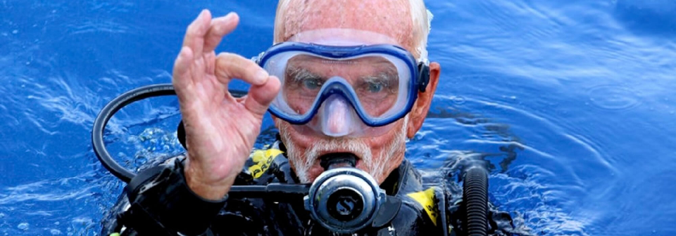 Scuba Instructor gently adjusting older client's gear, showing trust.